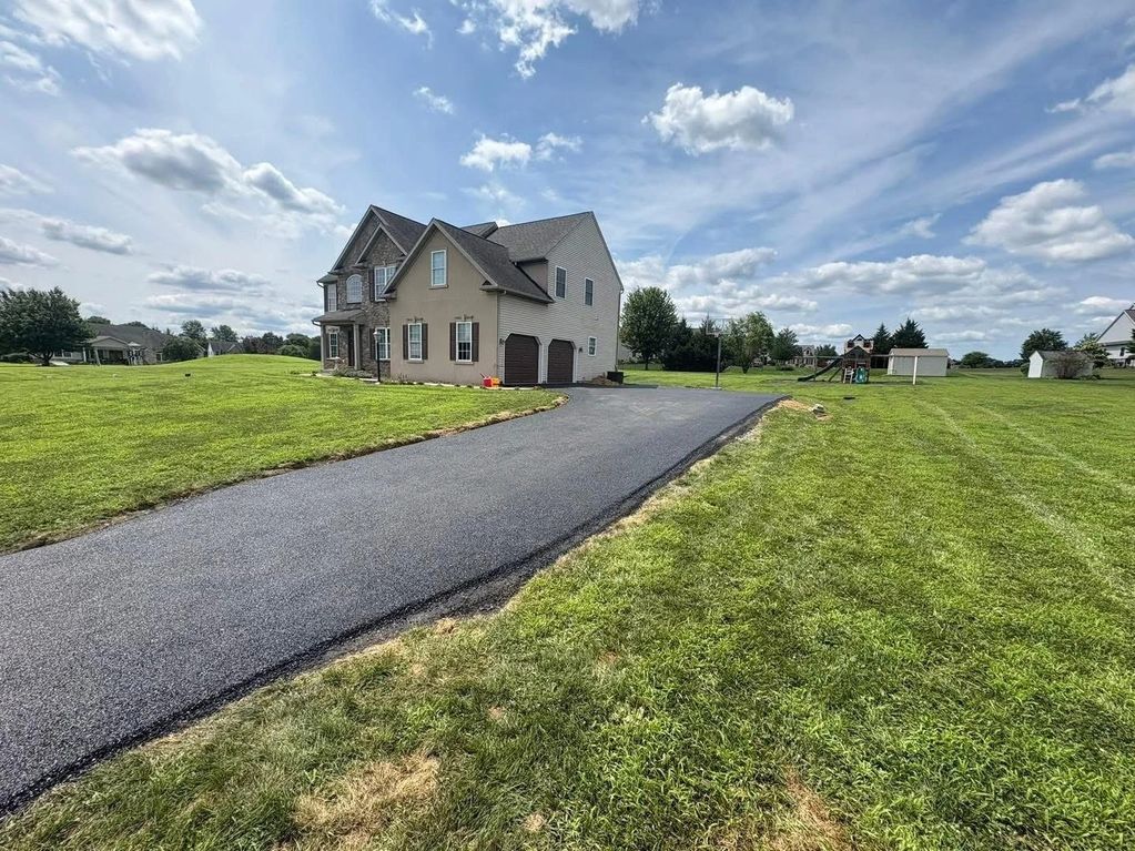 House with a long driveway and green lawn under a partly cloudy sky.
