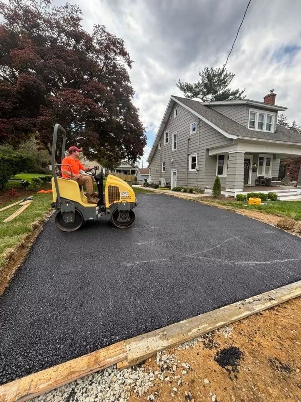 Worker paving a driveway with a small roller machine beside a house.