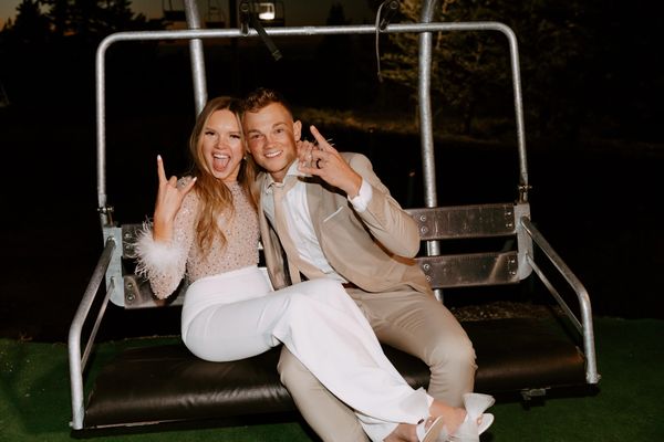 bride in her bridal jumpsuit on a ski lift with her groom at the end of their end night
