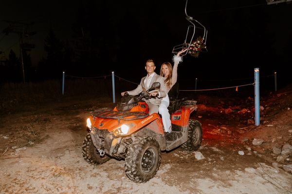 the bride and groom ride away from their wedding reception on a 4-wheeler ATV at dark