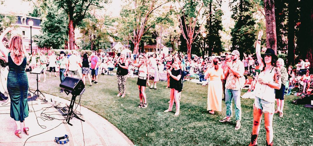 Outdoor concert with people enjoying music and dancing on grass.