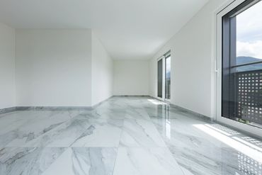 Empty room with glossy marble flooring and large windows letting in natural light.