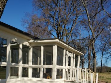 A sunlit white screened porch with steps and brick pathway on a sunny day.