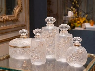 Elegant frosted glass containers with intricate gold floral designs on a reflective surface.