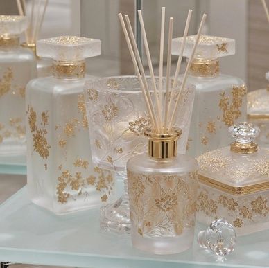 Elegant frosted glass perfume bottles with gold floral designs and reed diffuser sticks.