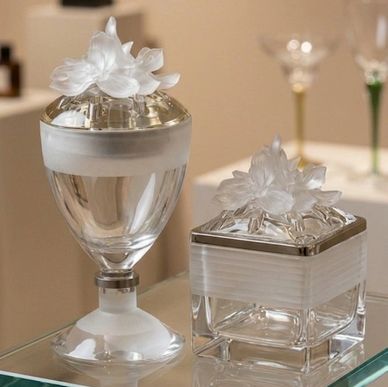 Elegant glass containers with floral lids displayed on a glass surface.