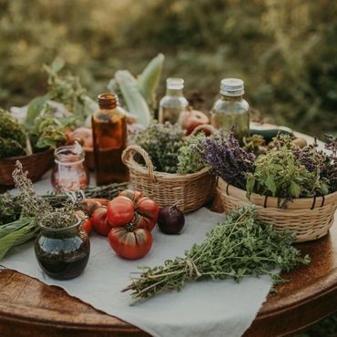 A rustic table with fresh herbs, tomatoes, and glass bottles outdoors.