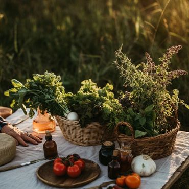 Fresh vegetables and herbs arranged on a picnic table outdoors at sunset.
