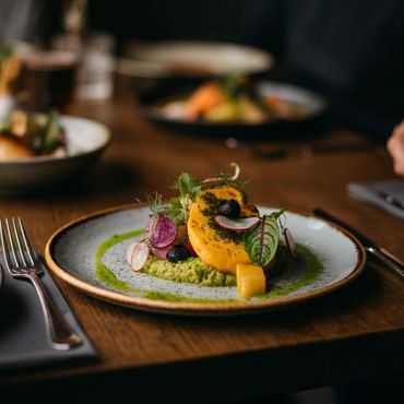 Gourmet dish with colorful vegetables and green puree on a ceramic plate.