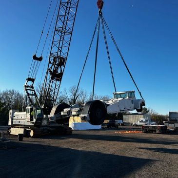 A crane lifting a heavy white vehicle component at a construction site.