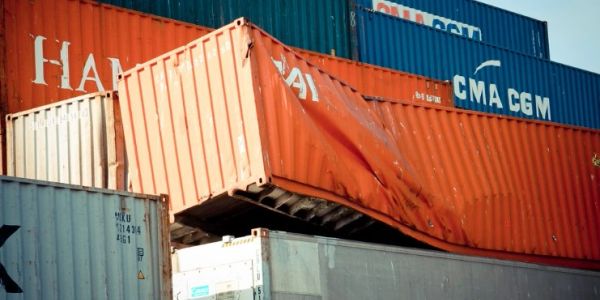 Damaged orange shipping container stacked among others at a port.