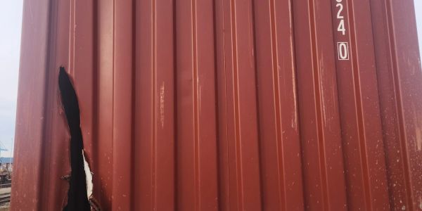 Large tear in a rusty red shipping container's side panel.