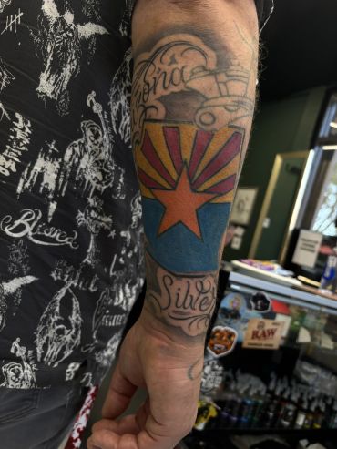 Tattoo of a colorful star and script on forearm.