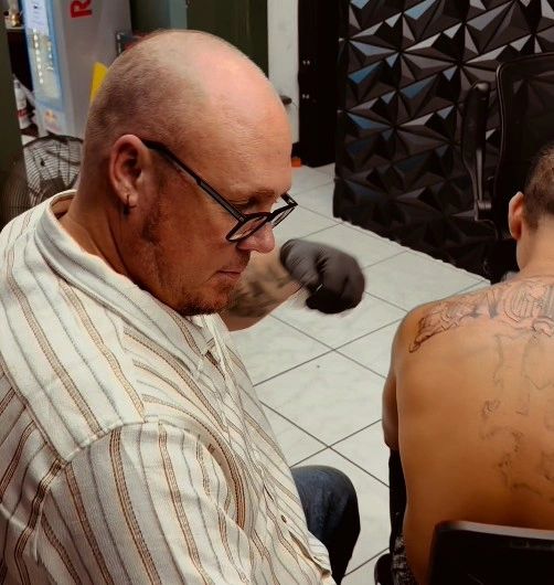 Tattoo artist working on a client's back tattoo in a studio.