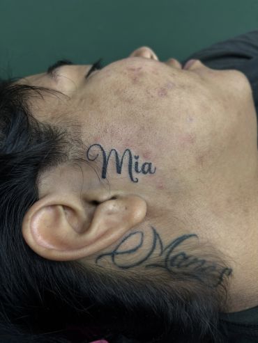 Side profile of a person with "Mia" tattoo on the side of the face.