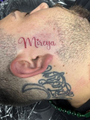 Red tattoo of the name Mireya on the side of a person's face.