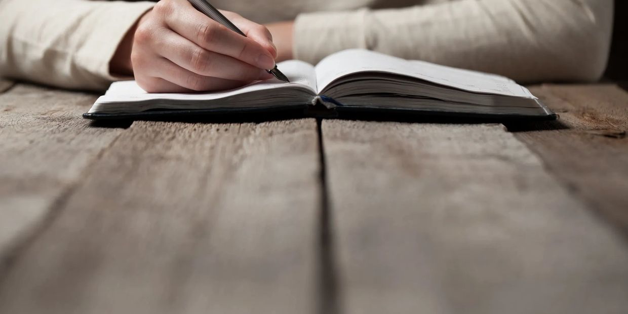 Close-up of a hand writing in a notebook on a rustic wooden table.