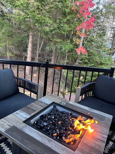 Cozy outdoor fire pit setup with two black cushioned chairs and a glass of white wine.