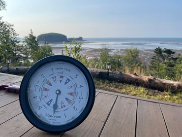 A tide clock on a wooden deck overlooking a coastal landscape with low tide visible.