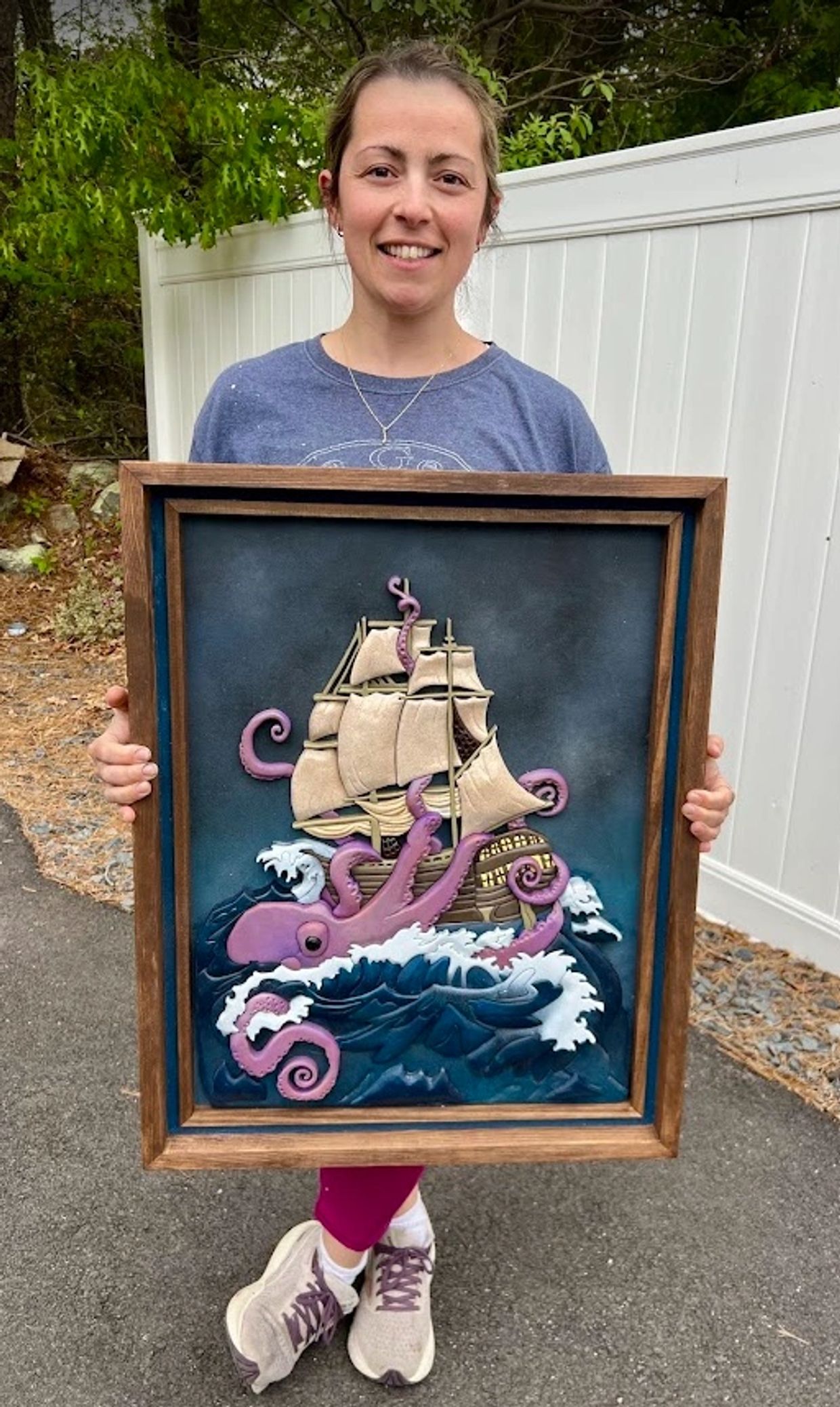 Woman holding framed artwork of a ship attacked by a giant purple octopus.