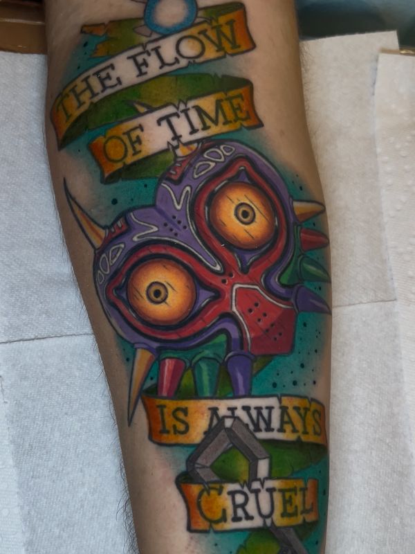 Colorful tattoo of Majora's Mask with phrase about time's cruelty.