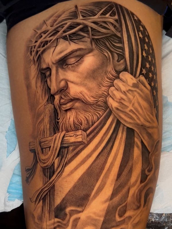 Detailed tattoo of Jesus with crown of thorns, American flag, and a wooden cross.