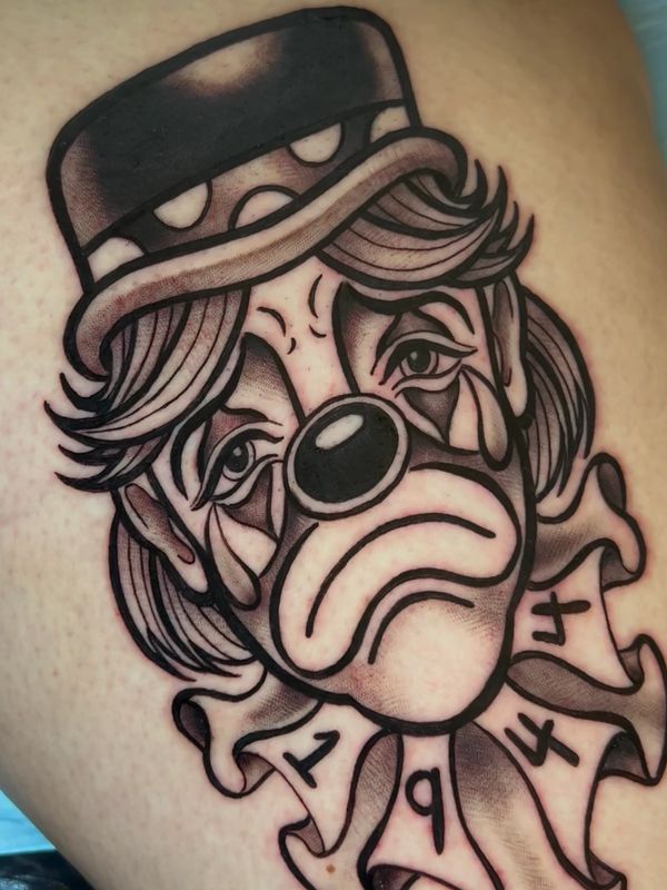 Tattoo of a sad clown with a hat and '194' on its collar.