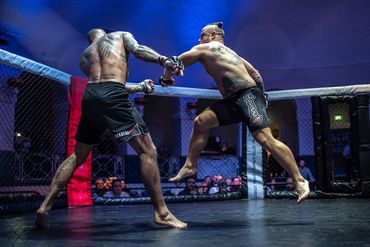 Two tattooed fighters engage in a mixed martial arts bout inside a cage.
