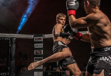 Two MMA fighters in a cage match, one delivering a high kick.