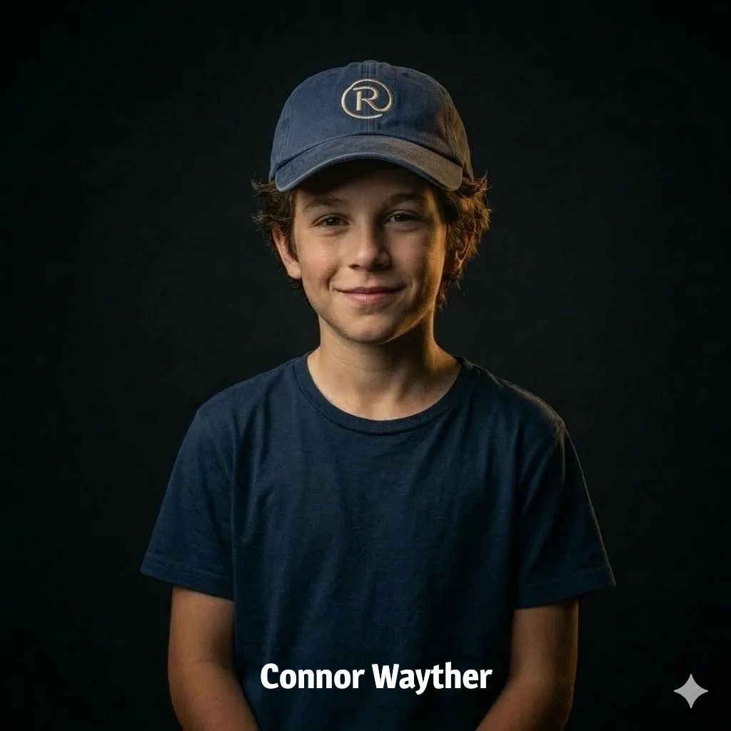 Young boy in a blue cap and shirt smiling against a dark background.