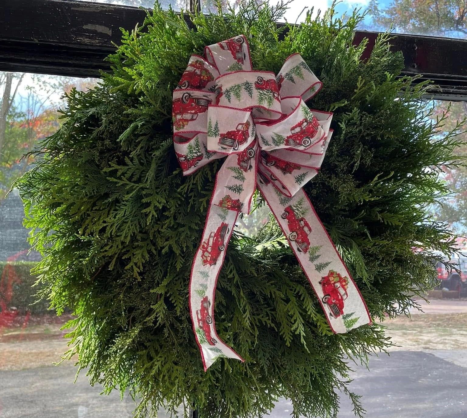 Green wreath with a festive bow featuring red trucks and pine trees.