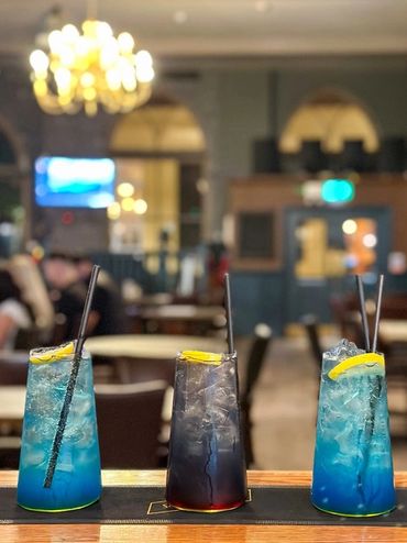 Three colorful cocktails with lemon garnishes on a bar counter.