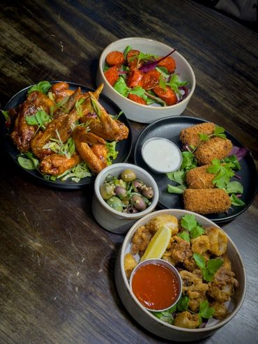 A variety of appetizers including wings, croquettes, olives, and fried bites with sauces.