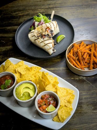 Grilled burrito with sides of sweet potato fries and nachos with salsa, guacamole, and pico de gallo.