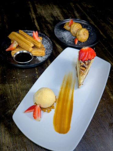 A trio of desserts artfully plated with strawberries and caramel sauce.