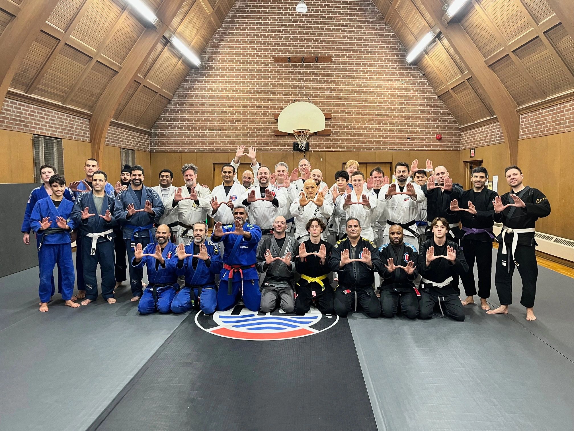 Group photo of martial artists in gis posing on mats inside a gym.