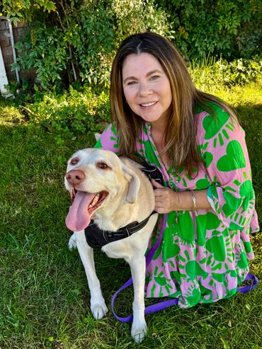 Smiling woman in colorful dress poses with happy dog in green garden.