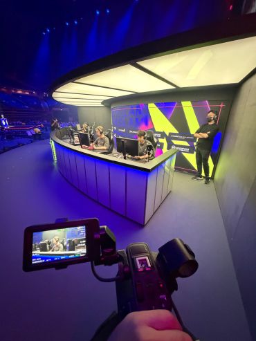 Esports players at an illuminated gaming event with a camera filming.