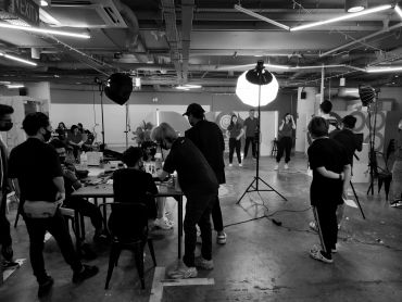 Photo shoot in progress with crew and models in studio.