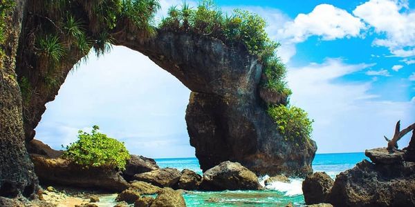 Natural rock arch over turquoise coastal waters under a bright blue sky.