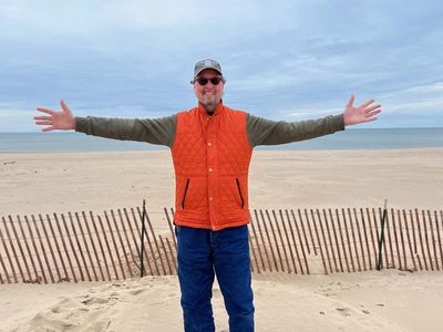 mike standing with outstretched arms on beach in front of snow fencing