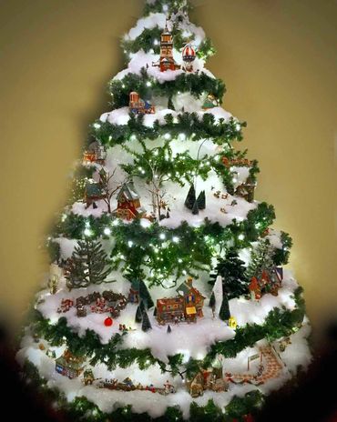 Christmas village set on large layered stand with realistic fake snow and garland with lights.