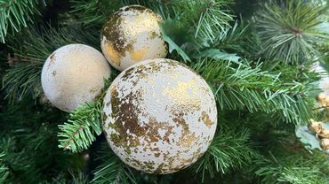 Hand-textured gold and vanilla bauble cluster with holly in branches on decorated Christmas tree.