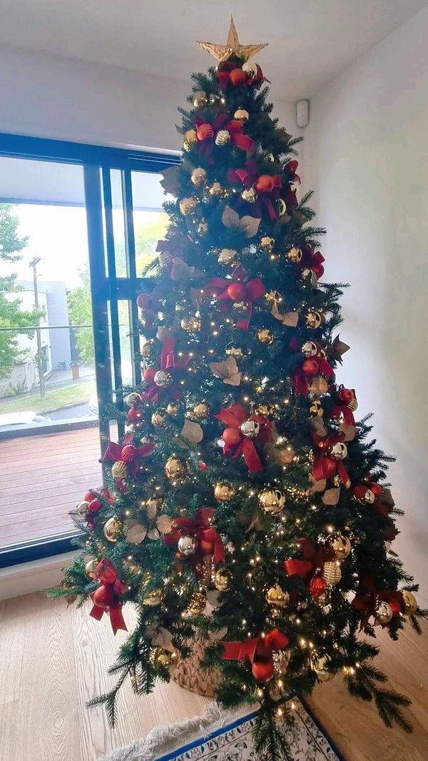Red and gold bow Christmas tree in home with fairy lights on.