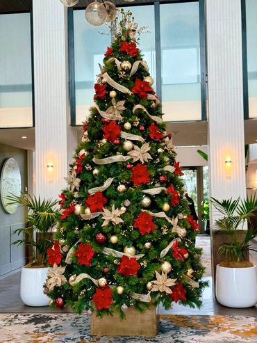 Hotel style Chrismtas decorations on 10 ft tall Christmas tree in foyer with red and gold flowers.