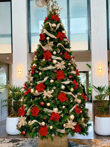 Hotel style Chrismtas decorations on 10 ft tall Christmas tree in foyer with red and gold flowers.