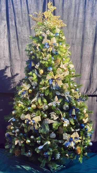Luxurious fully decorated Christmas tree with fancy blue and gold bows and cow bells plus ferns.