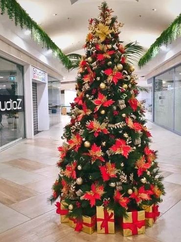 Bright red poinsettia flowers and gold decorations with berries on Christmas tree at shopping mall.