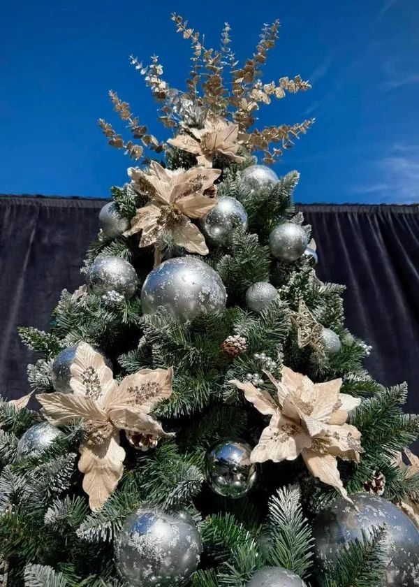 Closeup of artistic Christmas tree topper on champaign gold flower and silver bauble flocked tree.