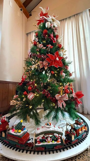 Small candy themed Christmas tree with gold holly and working toy train around base for party.